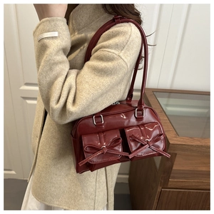 Close-up of glossy wine red patent leather shoulder bag with bow details and front pockets