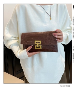 Detail of dark brown crocodile-embossed leather clutch with golden geometric lock buckle