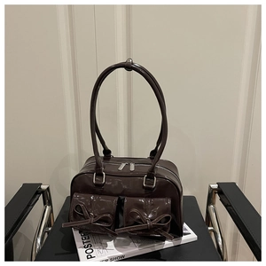 Macro shot of dark brown glossy shoulder bag with bow details and front pockets
