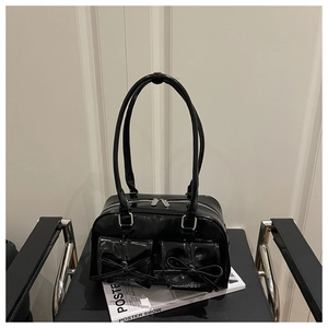 Close-up of black glossy patent leather shoulder bag with two bow-adorned front pockets