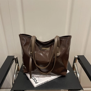 Fashionable dark brown high-gloss leather tote bag with elegant gold lettering on a chair