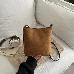 Vintage brown suede bucket bag with adjustable shoulder strap on white sofa
