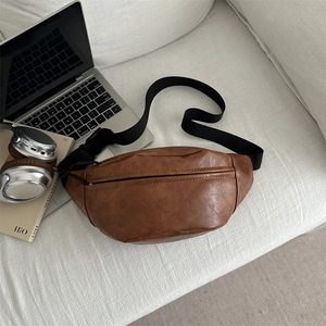 Minimalist vintage brown leather crossbody bag with adjustable strap on a sofa