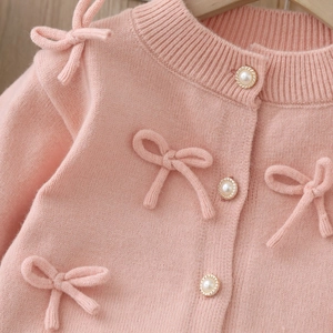 Dettaglio del cardigan in maglia rosa da bambina con bottoni di perle e fiocchi