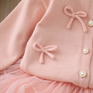 Dettaglio cardigan in maglia rosa con fiocco 3D e bottoni di perle con bordo dorato