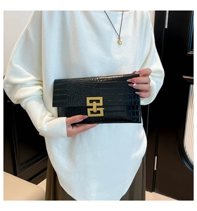 Detail of black crocodile pattern envelope clutch featuring a gold geometric clasp