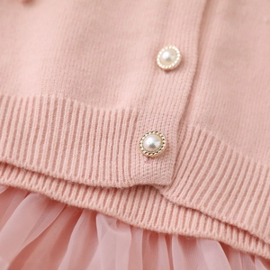 Dettaglio del cardigan in maglia rosa con bottoni a perla e bordo gonna tutu in tulle
