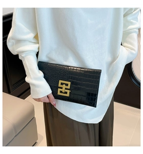Detail of black crocodile-embossed leather clutch featuring a gold interlocking clasp