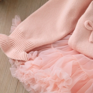 Dettaglio del cardigan in maglia rosa con fiocco e gonna in tulle a strati per bambine