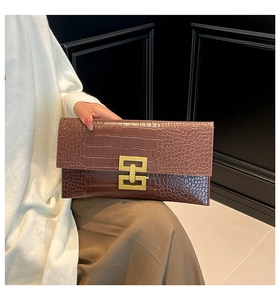 Detail of deep brown envelope clutch bag with crocodile texture and gold metal buckle