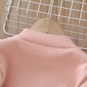 Dettaglio del colletto di un cardigan in maglia rosa morbido su una gruccia in legno