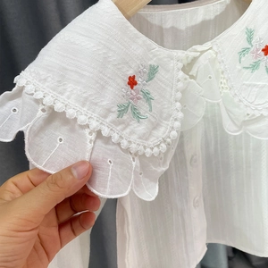 Détail d'un chemisier blanc pour fille avec broderies florales et dentelle sur le col