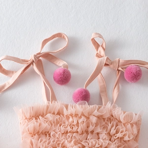 Detail of pink tutu dress featuring tie-up shoulder straps with fluffy hot pink pom-poms