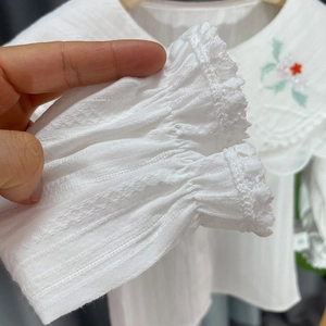 Détail de chemise blanche pour fille avec broderies florales et poignets dentelle élastique