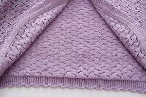 Detail of light purple knit fabric with delicate eyelet patterns and scalloped edges