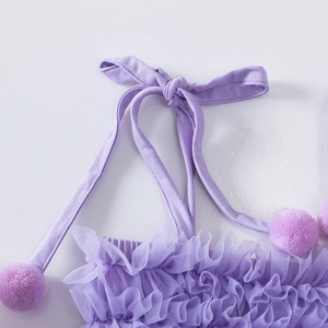Close-up of purple tutu dress featuring mesh ruffles, halter neck tie and fuzzy pom-poms