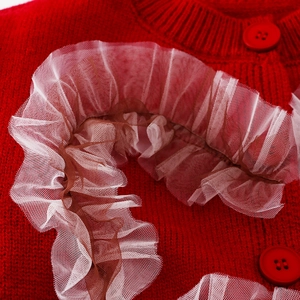 Detail der roten Strickjacke mit Rippkragen, runden Knöpfen und plissierter Netzspitze