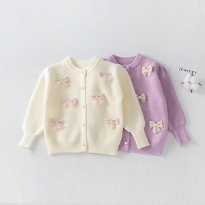 Detail of girl's knit cardigan featuring 3D tulle bows and elegant pearl buttons