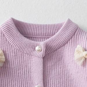 Detail of light purple knit cardigan with pearl button and lace bow accents