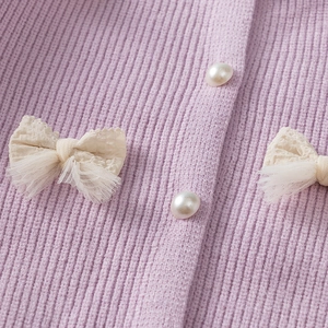 Detail of purple knit cardigan featuring lace bows and elegant pearl buttons