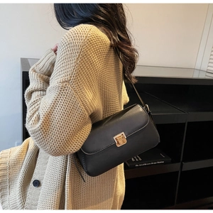 Dettaglio di una borsa a tracolla in pelle nera con fibbia dorata su una modella
