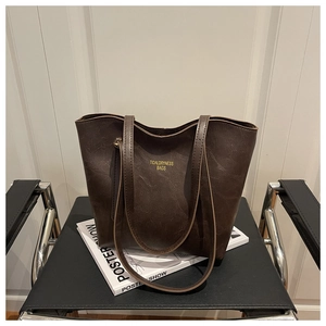 Detail of deep brown tote bag with gold lettering placed on a modern leather chair