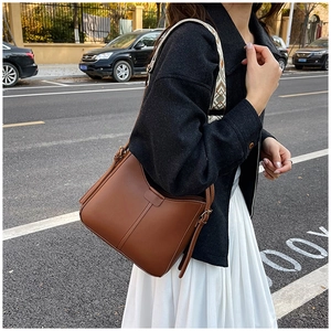 Brown leather crossbody bag with wide geometric woven strap shown in a city street setting