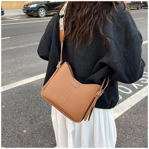 Caramel brown leather shoulder bag with ethnic patterned strap shown in an outdoor setting