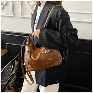 Détail du sac fourre-tout en cuir marron vintage avec poche à boucle et pompon porté par un mannequin