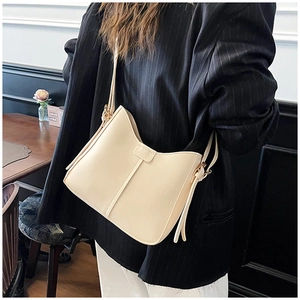 Side view of cream U-shaped shoulder bag featuring long zipper pulls in a cafe setting