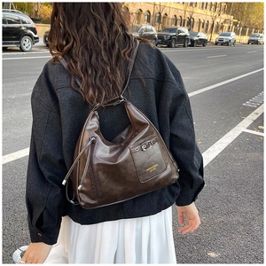 Détails d'un sac en cuir ciré marron foncé porté en sac à dos ou bandoulière par un modèle