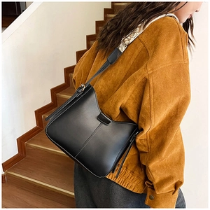 Détail du sac bandoulière en cuir noir mat avec large sangle géométrique porté par un modèle