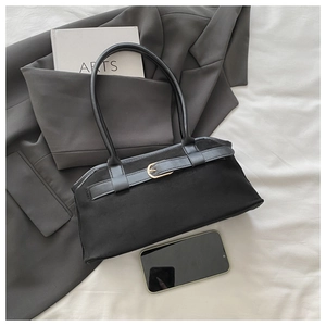 Detail view of black suede shoulder bag with gold buckle on a stylish suit backdrop