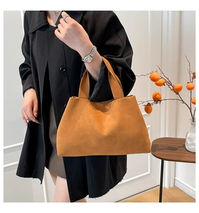 Close-up of a camel faux suede tote bag held by a model in a minimal indoor setting