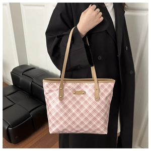 Detail of pink plaid tote bag with gold metal logo plate and brown leather handle