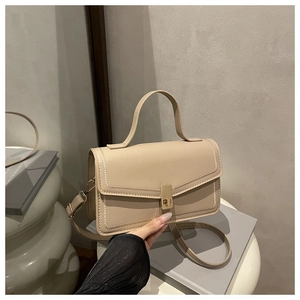 Detail of beige leather crossbody bag featuring gold metal clasp and decorative stitching