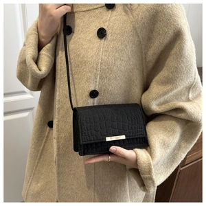 Détail du mini sac noir embossé crocodile avec boucle métallique sur un manteau beige