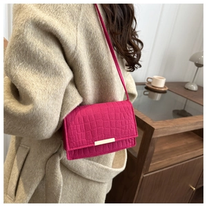 Gros plan sur un sac bandoulière rose rouge à motif crocodile et boucle dorée