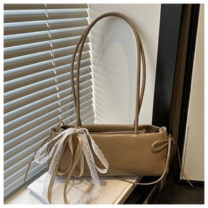 Detail of khaki shoulder bag with a large white lace bow and ribbons on book