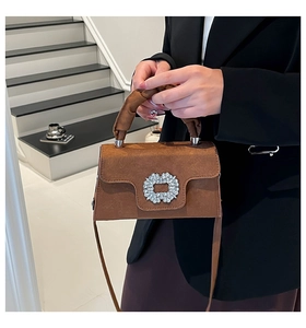 Detail of brown suede handbag featuring a large rectangular rhinestone buckle and carry handle