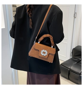Detail of brown suede crossbody bag featuring a crystal buckle and ruffled handle