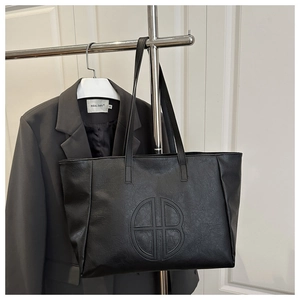 Detail of black faux leather tote bag with circular logo hanging in a casual setting