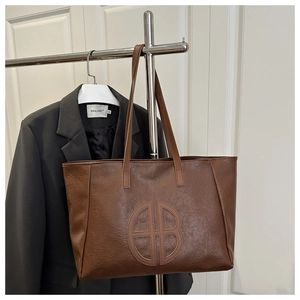 Detail of vintage brown leather tote bag with round quilted logo and long handles