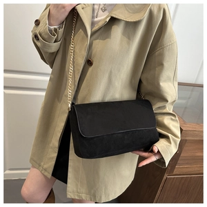 Detail of black suede crossbody bag with gold chain strap worn over a light coat