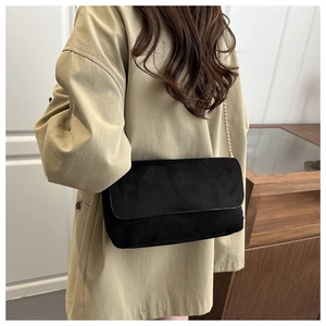 Detail of black suede crossbody bag featuring matte finish and gold chain strap