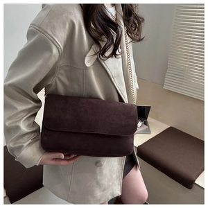 Close-up of a dark brown suede crossbody bag with golden chain strap on a model