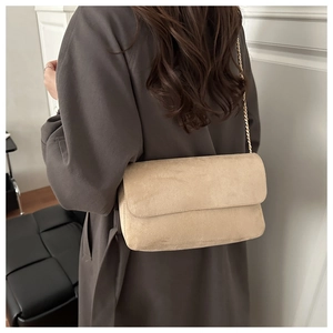 Detail of a beige suede crossbody bag with gold chain strap worn over a black coat