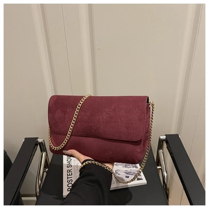 Close-up of wine red suede crossbody bag featuring a sleek flat gold chain strap
