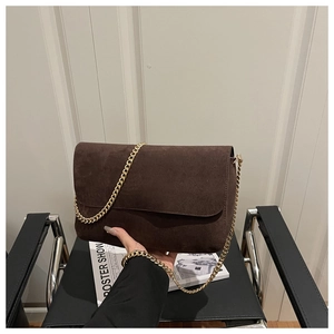 Close-up of a dark brown suede handbag with a luxury golden chain strap and flap closure