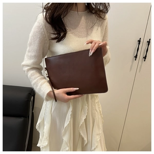 Close-up of a stylish dark brown pleated clutch held by a model in casual chic attire